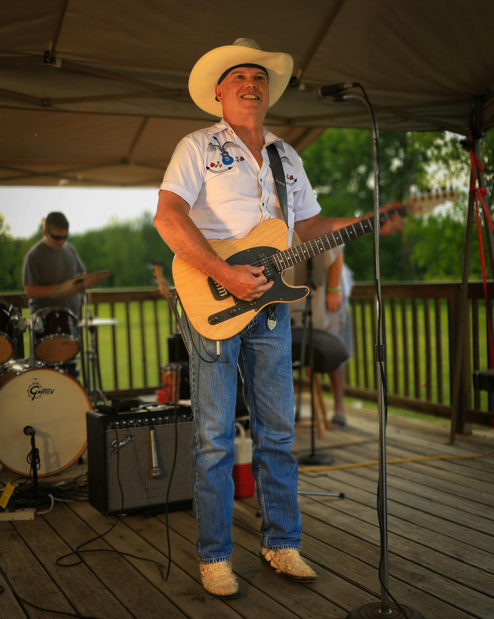 A musician in a cowboy hat performs guitar on stage during a lively outdoor event.