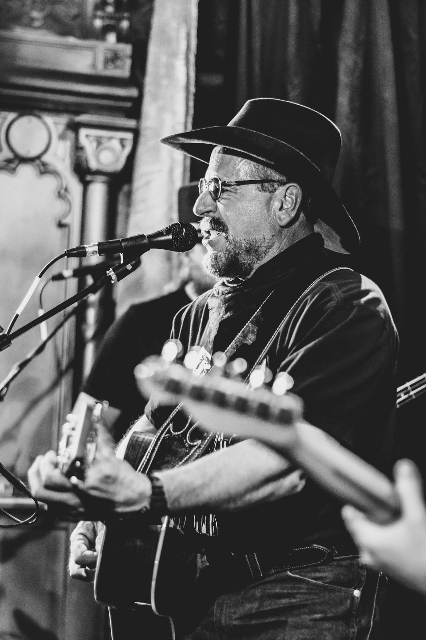 Black and white photo of a musician singing and playing guitar on stage.